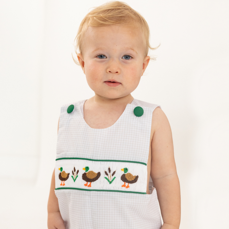 Baby wearing a white sleeveless top with duck design on a plain background